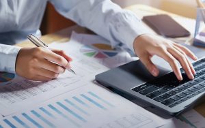 Accountant typing on laptop while analyzing financial bookkeeping reports.